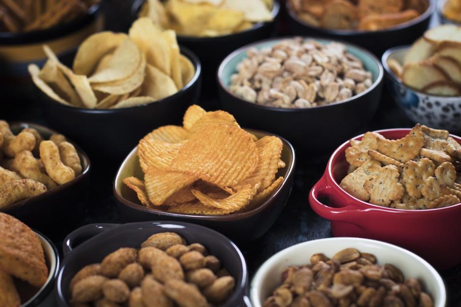 Various shaped bowls filled with various snacks including chips, nuts, crackers