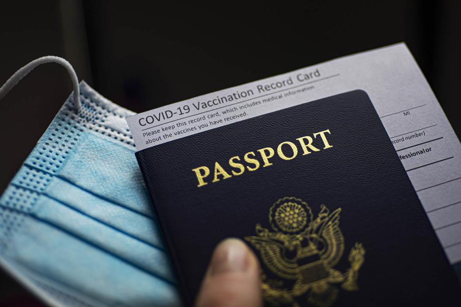 Hand holding a US passport, Vaccine card sticking out of the passport, and mask
