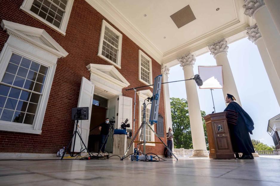 President Jim Ryan standing under the cover of the Rotunda at a podium in graduation robe and hat with a film crew filming him