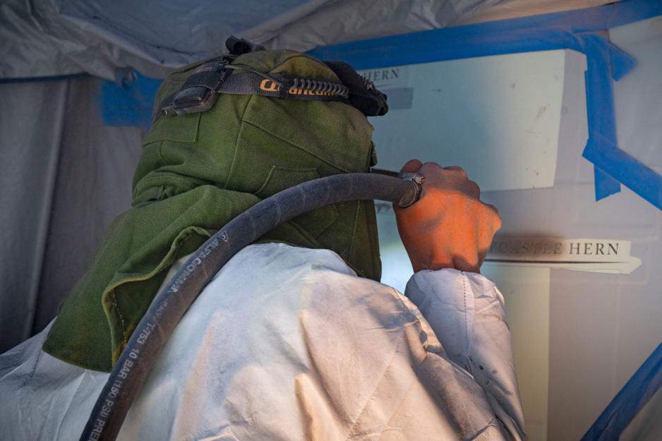 Man in protective gear spraying a brown paint like substance over a stencil on the wall