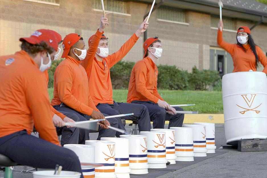 Percussionists drumming on UVA branded buckets while one member has both drumsticks in the air 
