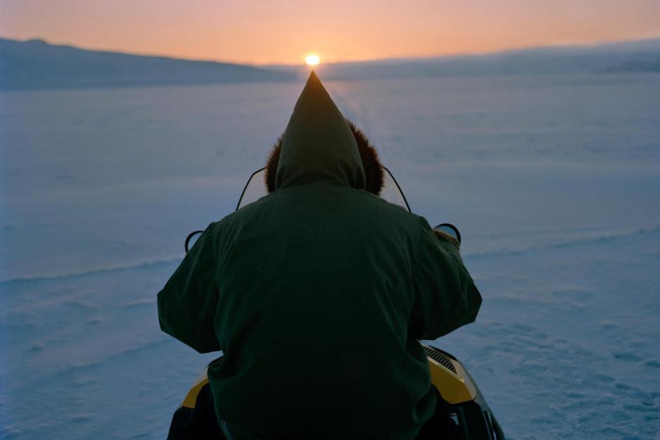 An Inuit man driving a snow mobile at night