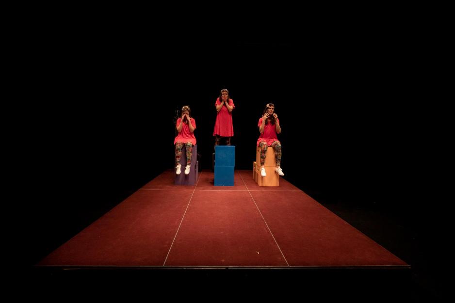 Left to right, Sarah Rabke, Melissa Frost and Alicia Lopez Operé sit on multicolored boxes in the spotlight