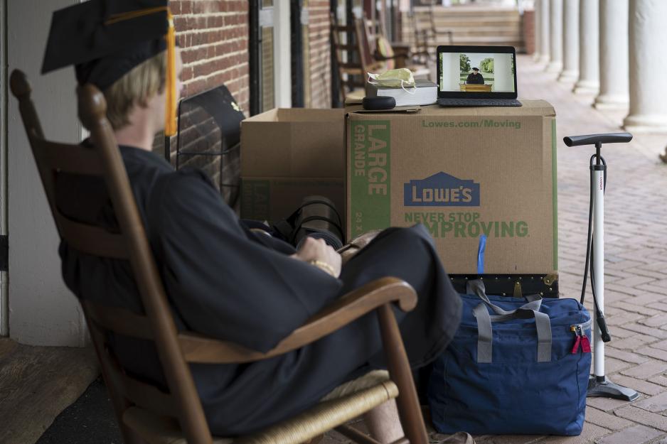 Graduate sitting outside of their room on the Lawn in their cap and gown watching the commencement speech 