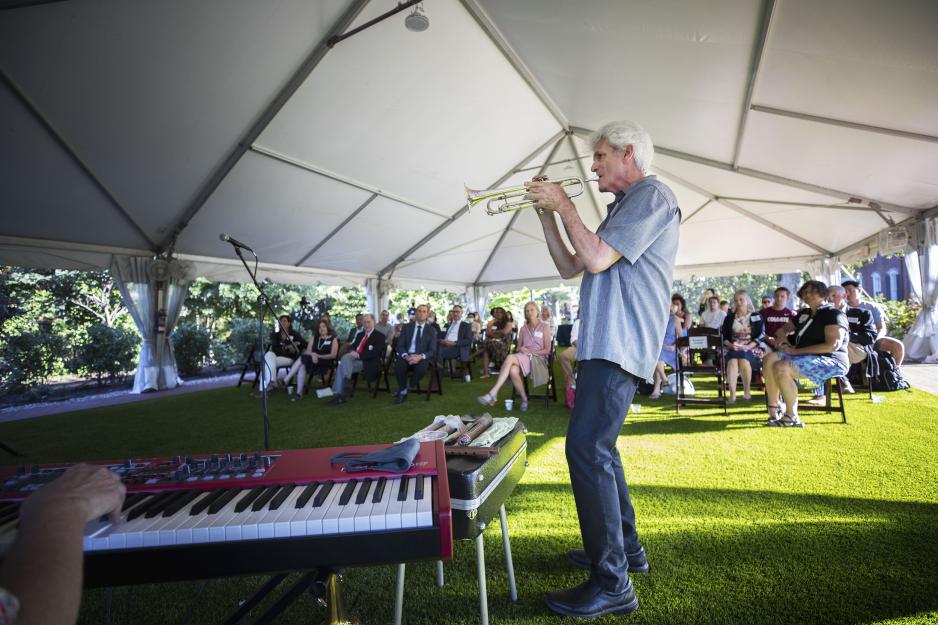 Man standing and playing trumpet while an audience sits and watches