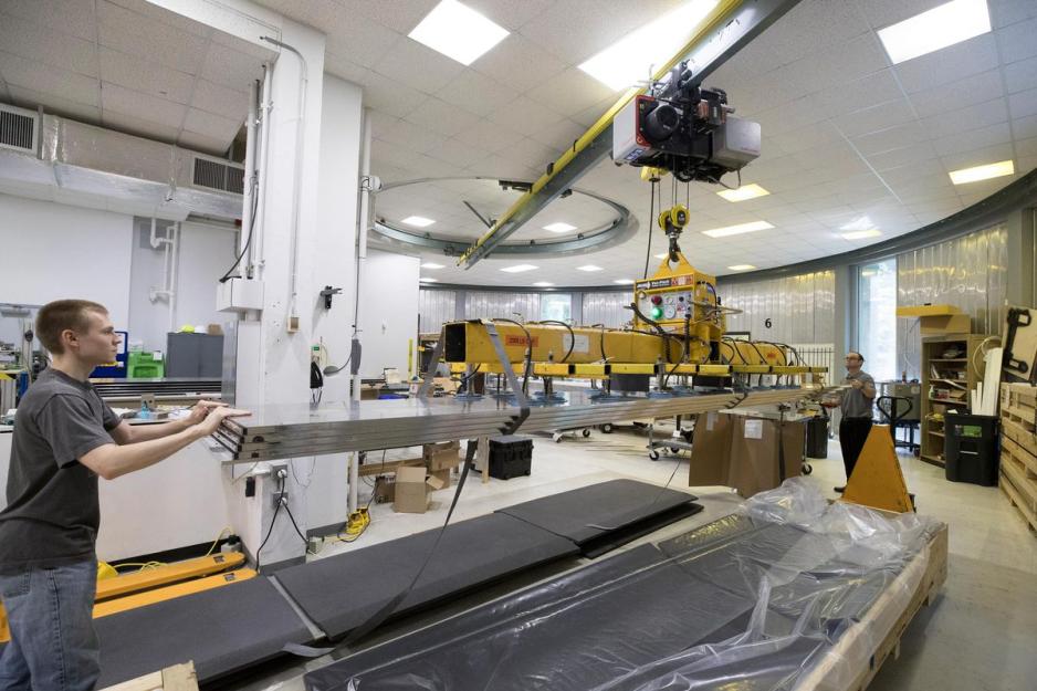two students help guide a machine carrying metal slabs