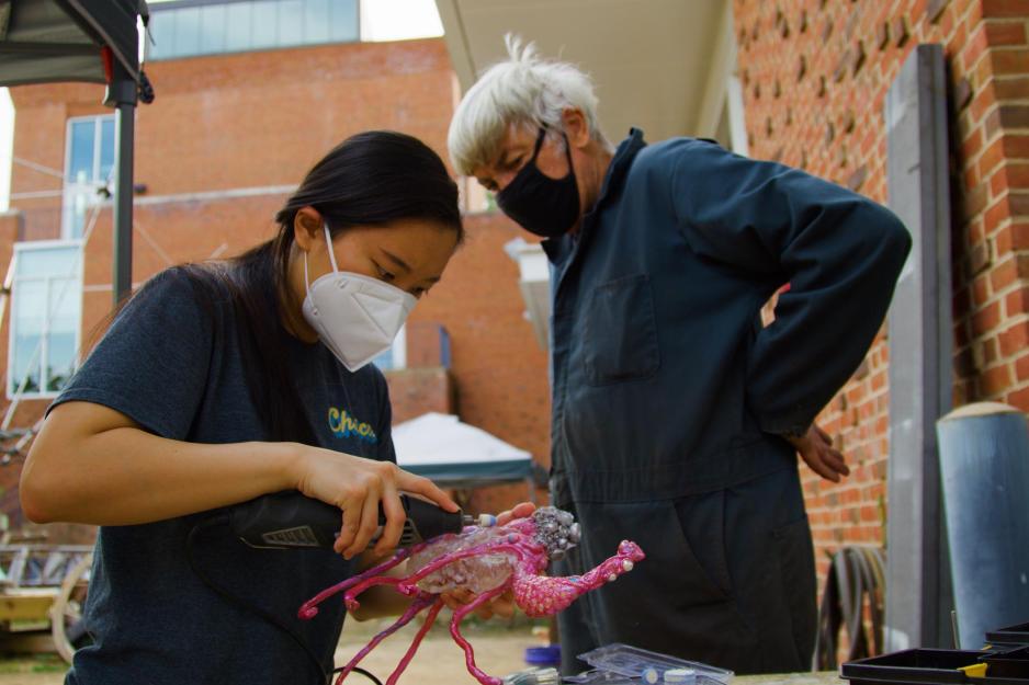 Student working on a sculpture while professor watches