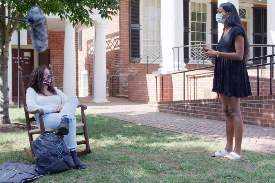 Student sitting in wooden rocker, left, while another student stands 6ft away talking to them