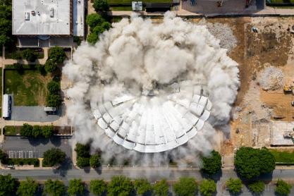 Aerial view of UHall being imploded with dust and smoke coming out 