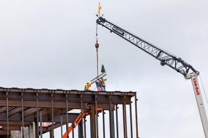 Construction workers guiding a beam being craned onto the top of a building
