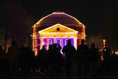 crowd watching the University of Virginia Rotunda illuminated with colorful lights and holiday decorations at night.