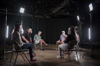 Five people wearing face shields sit in a circle in a television studio