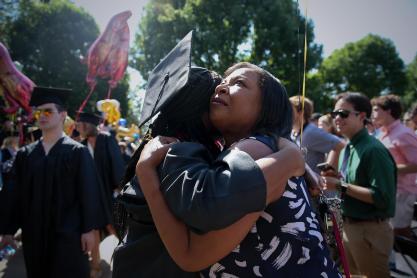 A woman holding back tears embraces a graduating student.