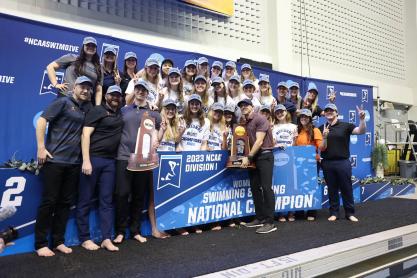 The UVA Women's Swim and Dive team with their coaches posing together with their NCAA championship trophy