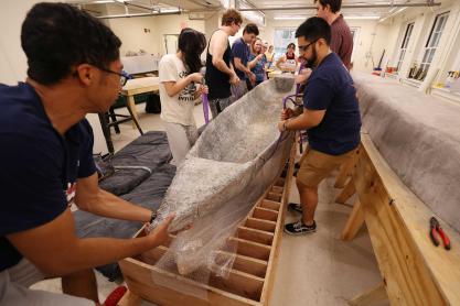 Students handle concrete boat on its stand