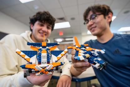 Two students holding orange, blue, and white custom Lego planes