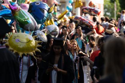 A 2025 graduate pauses in the procession to give a joyful smile and wave to their family