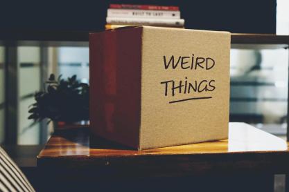 A cardboard moving box labeled 'Weird Things' rests on a coffee table