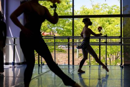 Silhouettes of ballet dancers backdropped against floor-to-ceiling windows in a dance studio