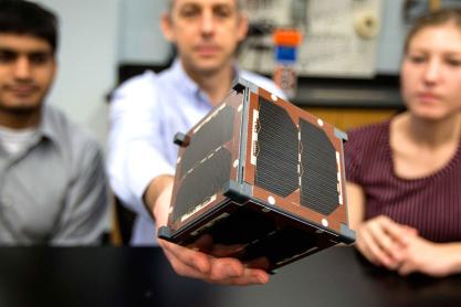Chris Goyne, center, and students Chandrakanth “C.K.” Venigalla, left, and Robin Leiter hold a mini satellite for a NASA experiment.