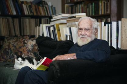 Jim Kavanaugh sitting on his couch with his black and white cat and book