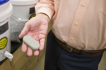 Man holding an grey oval MadiDrop tablet in their hand