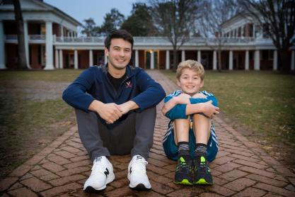 Liam Flaherty, left, and Jasper, right, sit on a sidewalk on the Lawn with the knees up, elbows on knees smiling for the camera
