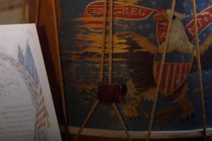 up close view of an old painting on wood with an eagle and ropes holding the wooden picture in place