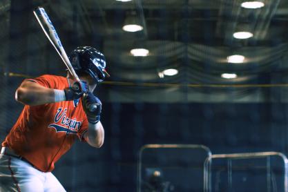 UVA baseball player preparing to hit a ball with the bat up near his shoulder as a machine is throwing at him