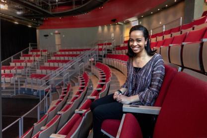 Jessica Harris sits in a red theatre chair looking at the camera smiling