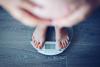 A pregnant woman weighs herself on a digital scale.