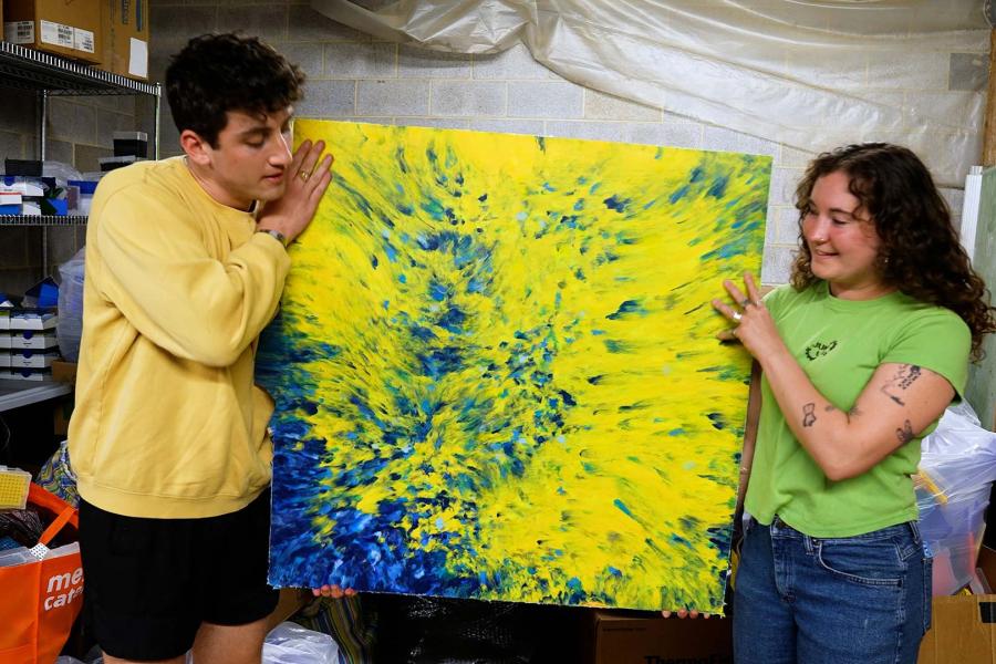 Two students displaying a piece of art created from trash.
