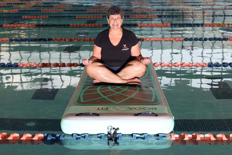 Ellen Goldlust sitting on an inflatable yoga mat at the UVA Recreation pool during aqua yoga instruction.