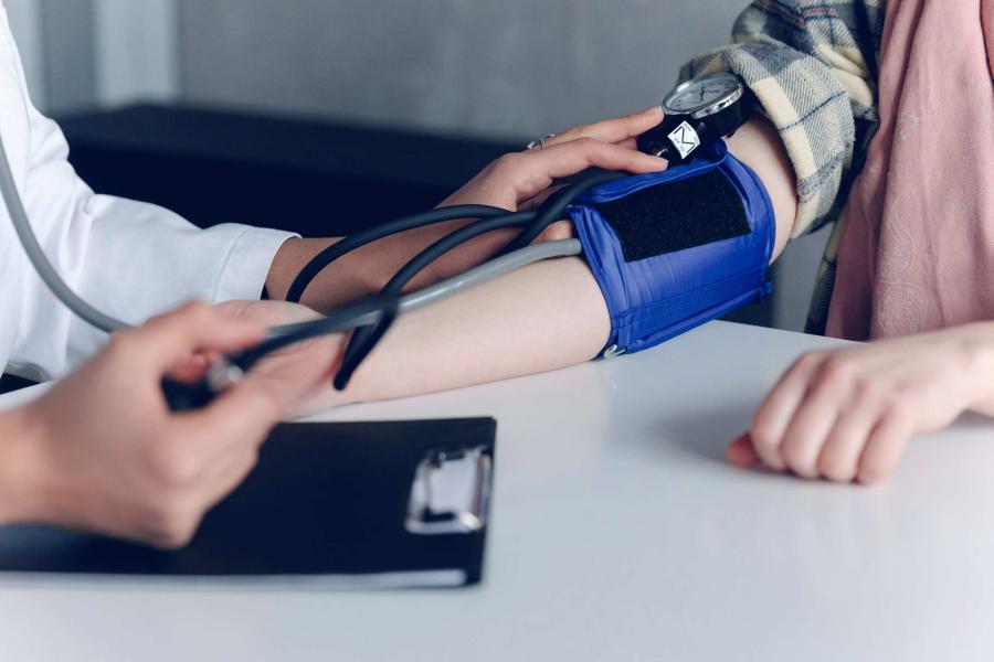 a patient wearing a blood pressure cuff while a medical professional monitors with a stethoscope.