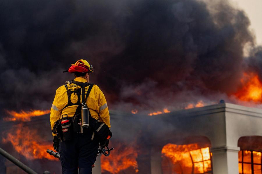 A lone firefighter stands in front of a massive fire in California