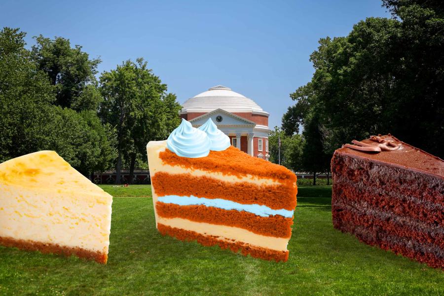 Three oversized slices of cake — cheesecake, red velvet with blue frosting, and chocolate cake — placed on a green lawn in front of the Rotunda at the University of Virginia, with trees and a clear blue sky in the background.