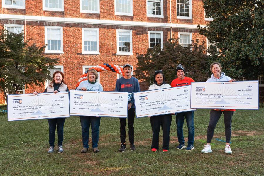 President Jim RYan and others stand and hold 4 giant checks