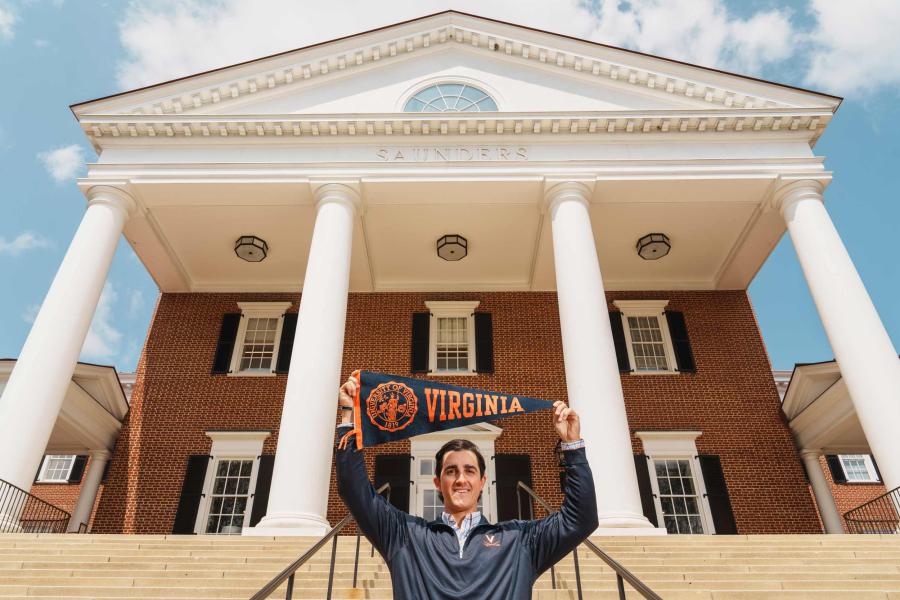 Andrew Katz standing in front of the UVA Rotunda holding a Virginia pennant over their head