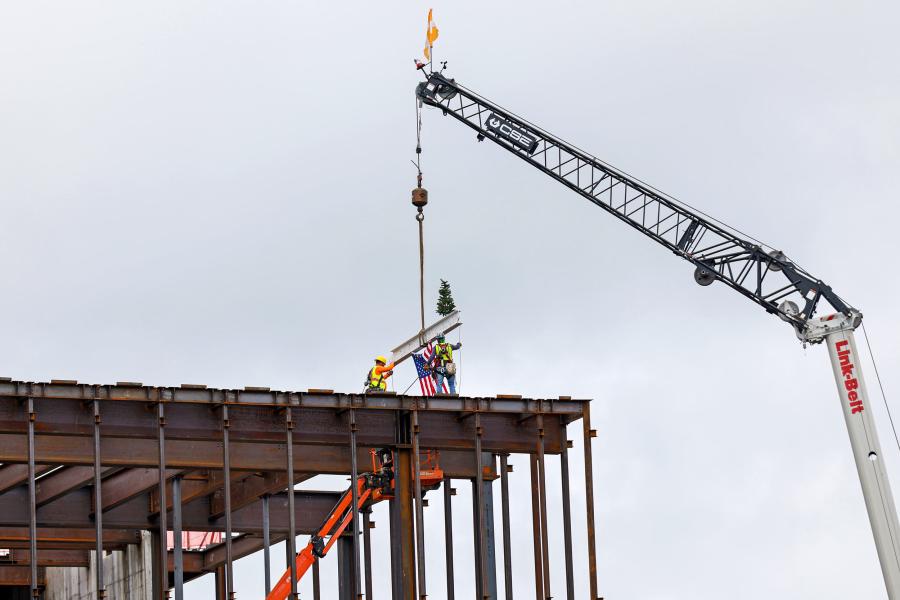 Construction workers guiding a beam being craned onto the top of a building