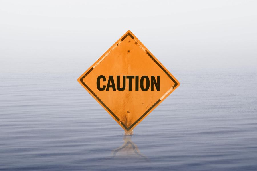 a diamond-shaped caution road sign is barely visible in rising flood water