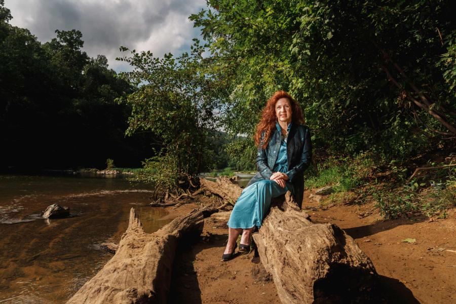 Robin Dunbar sitting on a log on the shore of the Elizabeth River