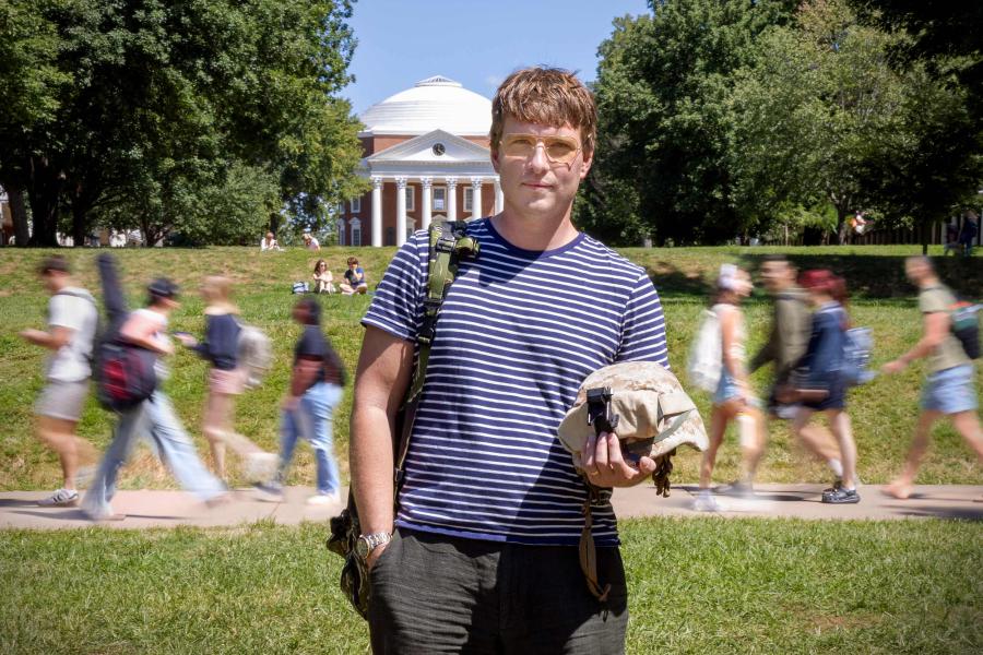 Stephen Cantry wearing a Marines backpack and headwear stands for a photo on the Lawn in front of the Rotunda at UVA on a bright afternoon