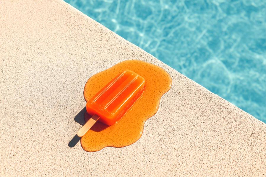 an orange popsicle melting by a swimming pool