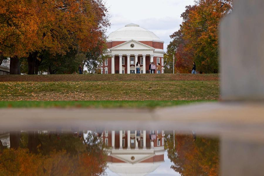the UVA Rotunda being reflected in a pool of water. There are students congregating on the Lawn in front of the Rotunda.
