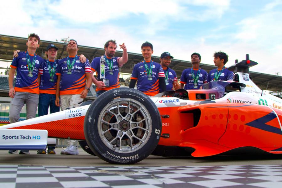 The race car team stands behind the car