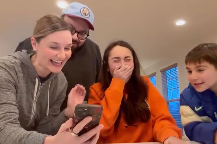 Portrait of a family showing their daughter a mobile phone with the results of her admission to the University of Virginia.