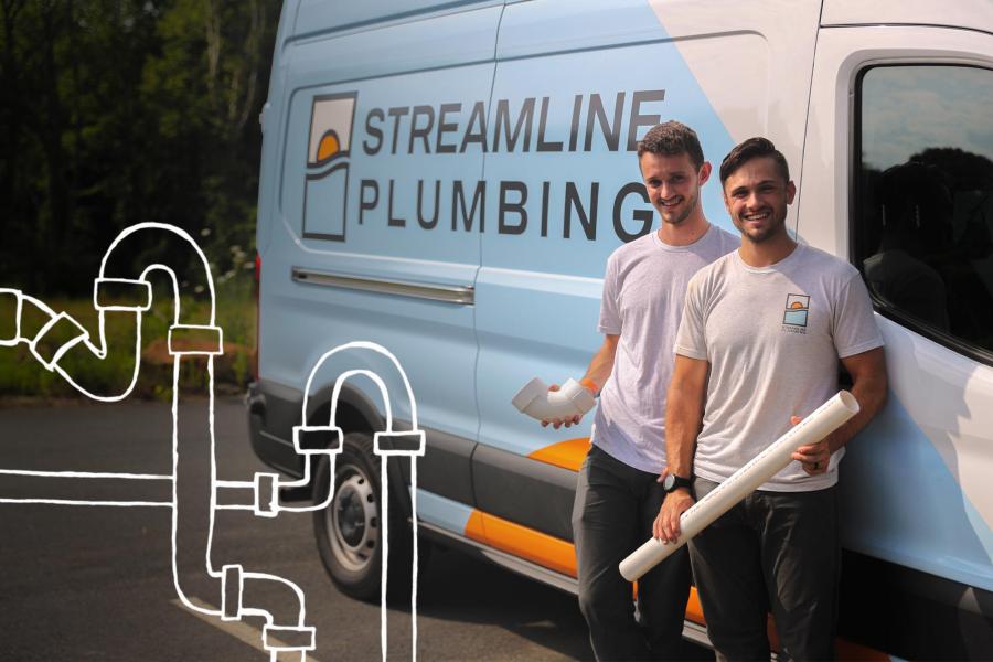 Two men in holding PVC pipes lean against a van with the words Streamline Plumbing on the side