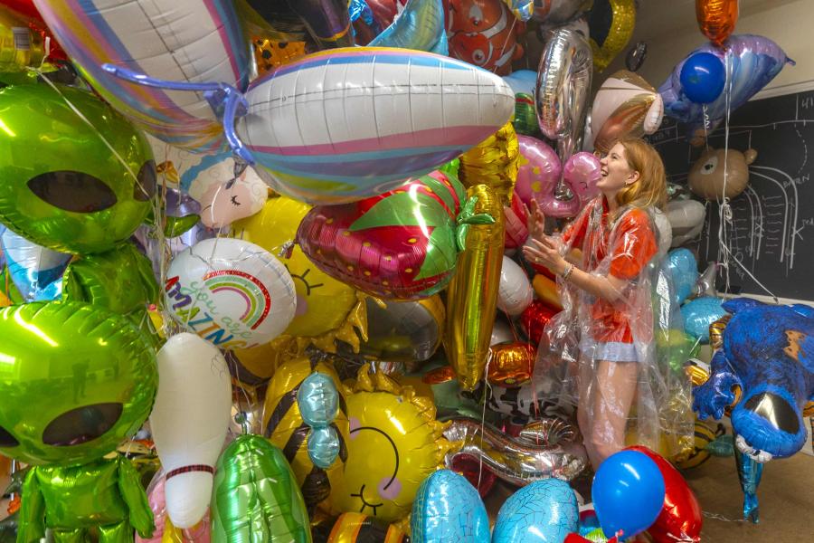 A mass of balloons looms over a volunteer balloon wrangler in a hallway of old cabbell