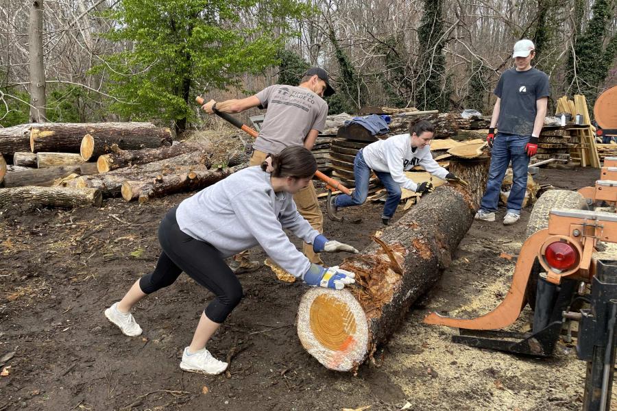 Two School of Architecture graduates and a student work together to move a log