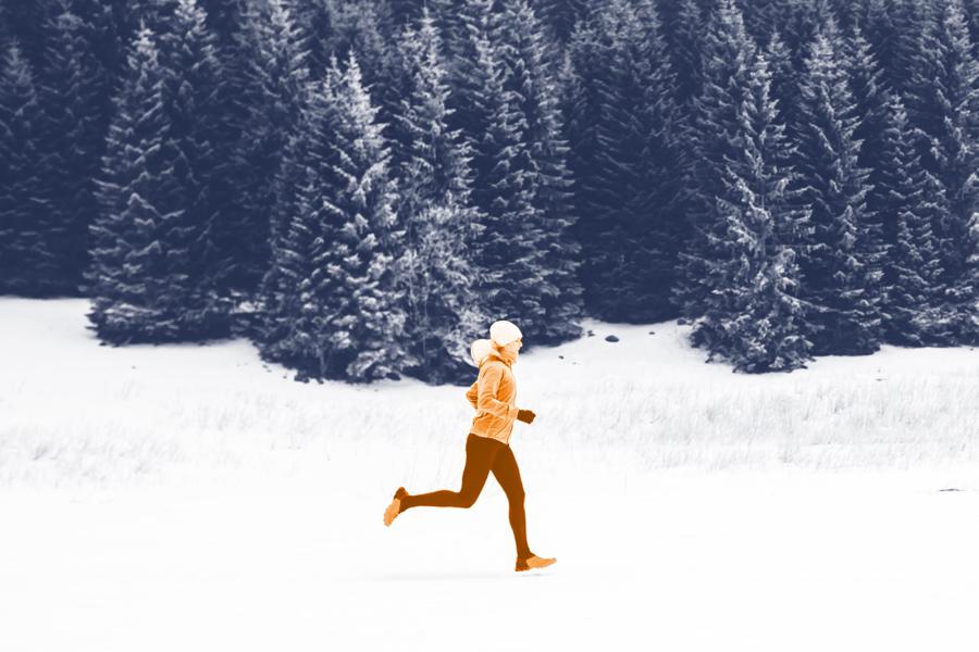 Runner running in the snow through an evergreen forest